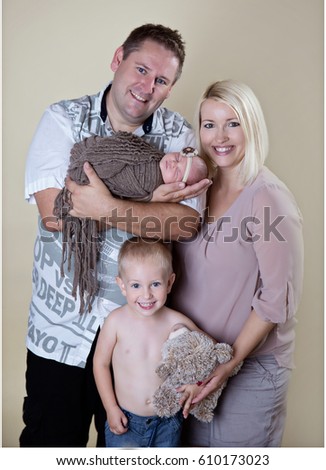 A beautiful family is having a professional photo-shoot together. A toddler is holding a teddy bear in his hands and a baby girl is sleeping in her father's hands.