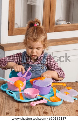 little girl playing toy baby dishes at home