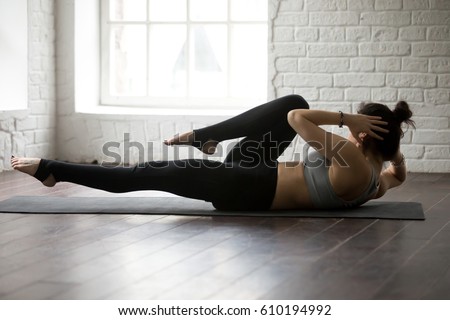 Young attractive cool sporty woman doing crisscross fitness exercise, bicycle crunches, working out on the floor, wearing black sportswear bra and black pants, full length at home or sports center  Royalty-Free Stock Photo #610194992