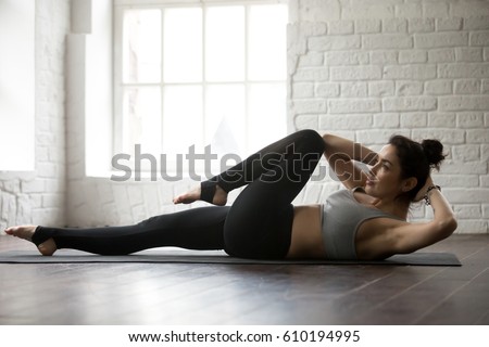 Young attractive cool sporty woman doing crisscross fitness exercise, bicycle crunches, working out on the floor, wearing black sportswear bra and black pants, full length white loft studio background Royalty-Free Stock Photo #610194995