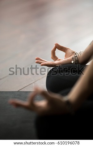 Close up of mudra gesture, performed with female fingers, yogi woman meditating in lotus pose, wearing wrist bracelet, sitting in Padmasana exercise, vertical photo. Meditation session concept  Royalty-Free Stock Photo #610196078
