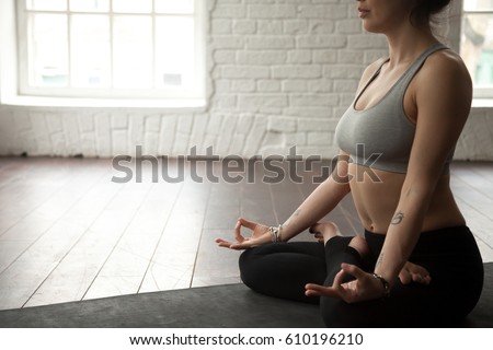 Young cool attractive yogi woman practicing yoga concept, sitting in Padmasana exercise, Lotus pose, working out, wearing sportswear bra and pants, midsection close up, white loft studio background  Royalty-Free Stock Photo #610196210