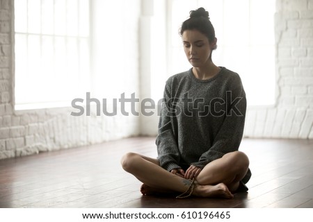 Young calm yogi woman practicing yoga concept, sitting in Sukhasana exercise, Easy Seat pose, her eyes closed, working out wearing grey oversized sweater, beads in hands, full length studio background Royalty-Free Stock Photo #610196465