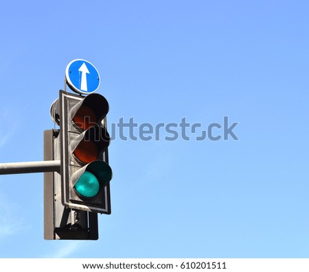 Green traffic light with straight forward arrow sign above, blue sky background