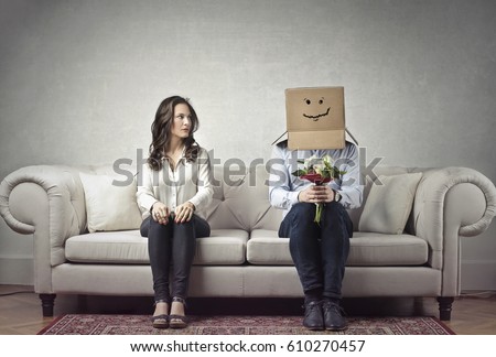 Shy man sitting next to a woman with his head covered by a cardboard box Royalty-Free Stock Photo #610270457