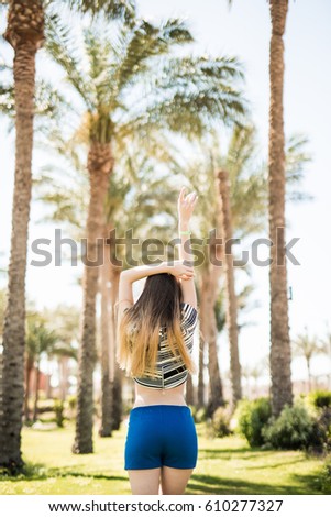Back view of happy excited young woman with raised hands walking and enjoying on summer resort