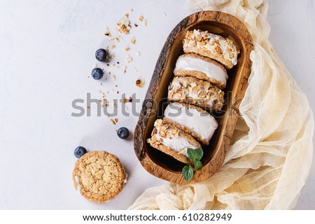 Set of homemade ice cream sandwiches in oat cookies with almond sugar crumbs, blueberries and mint on in olive wooden bowl over gray texture background. Top view with space