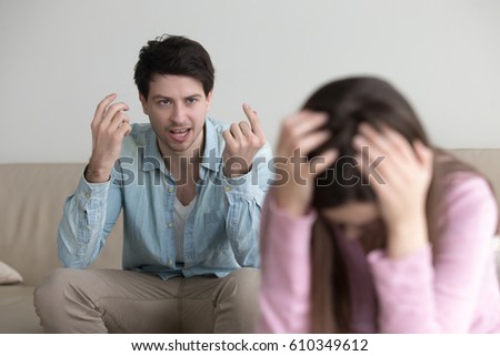 Young couple quarrelling at home, aggressive boyfriend yelling at sad lady, upset girl sitting silent holding head in hands. Mad guy accusing girlfriend of cheating. Family relationship problems  Royalty-Free Stock Photo #610349612