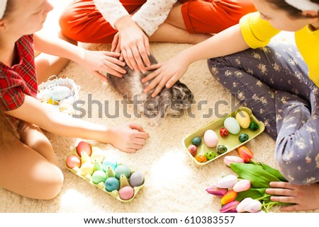 Girlfriends  in bunny ears sitting on the floor and playing with Easter rabbit. The concept of preparation for Holiday