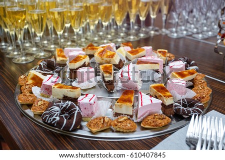Different delicious desserts and cakes on the buffet table against the background glasses with champagne