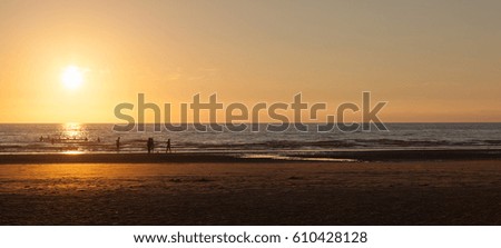 a large family, silhouetted by the setting sun, at play on the shore and in the sea at Blackpool, england