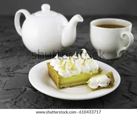 Lemon meringue pie, cup of tea, white  teapot gray cement table. Horizontal, selective focus.
