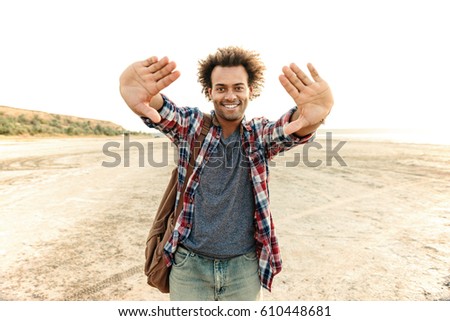 Cheerful african man with backpack focusing by his hands on the beach