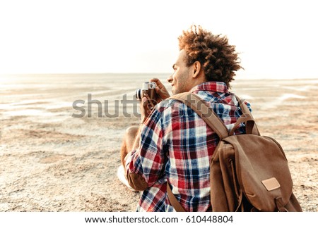 Back view of happy african young man taking pictures on the beach