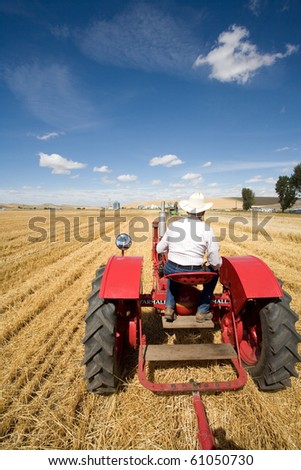 A man in a cowboy hat drives a tractor in a field. Royalty-Free Stock Photo #61050730
