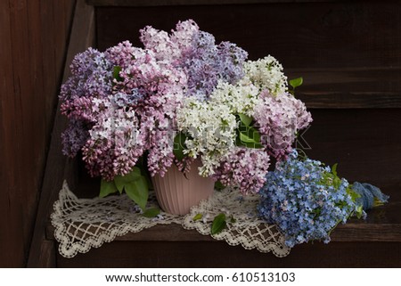 A bouquet of lilac flowers in a vase and forget me not flowers on the steps of a wooden staircase