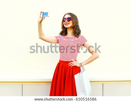Fashion pretty smiling woman takes a picture on smartphone with shopping bag over white background