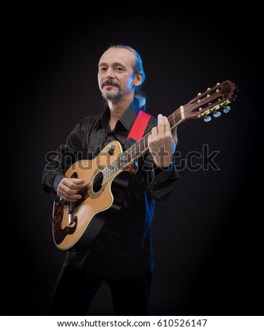 An elderly gray-haired male musician with long hair with a guitar in his hands playing and posing on a black background in a blue scenic light