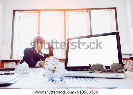 Blank screen laptop and office equipment on desk with blurred background of businessman hard think on the analysis in the work

