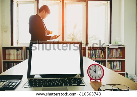 Blank screen laptop and office equipment on desk with blurred background of businessman work until coffee break
