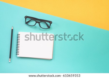 Flat lay design of work desk with notebook and glasses on green and yellow background. 