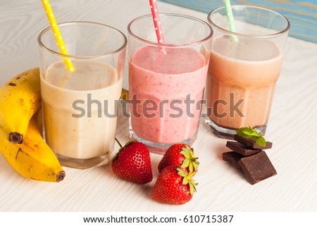 Long glasses of milkshakes with chocolate, strawberry, banana, with ice cream on white and blue background. Shakes and smoothies. Milk shake and cocktail for summer.