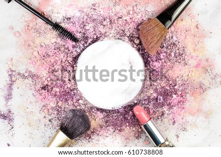 Makeup brushes, lipstick, and mascara applicator on white marble background, with traces of powder and blush forming frame. Horizontal template for makeup artist's business card, with copy space