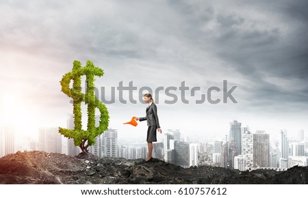 Young attractive businesswoman watering plant in ground with can against the backdrop of the city