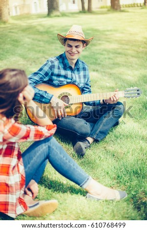 A beautiful, loving couple in cowboy style is having a good time. Guy plays the guitar outdoors in park