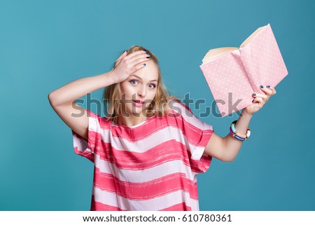 young attractive blond woman holding pink book on blue background