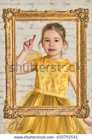 Indoor portrait of an expressive adorable young little girl seen from an wooden carved frame. Face gesturing, miming, acting
