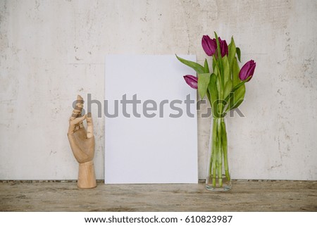 White mock up frame with wooden hand for drawing and fresh tulips. Textured cement wall, wooden desk. Interior photo