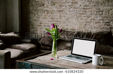 Laptop mockup with bunch of tulips and cup of coffee on textured old wooden table in room. Interior styled photo