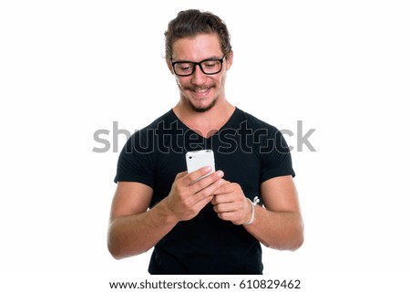 Studio shot of young happy man smiling while using mobile phone with eyeglasses isolated against white background
