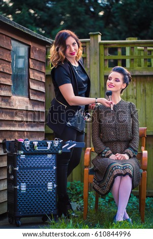 Makeup artist corrects makeup on a face of stylish woman who sits on chair outdoor