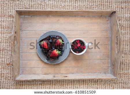 photo of delicious tasty muffins with blueberries and fresh strawberries on the top and cup of tea with petals on the board on the wonderful brown carpet background