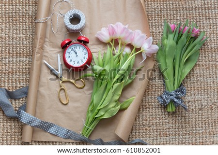 photo of beautiful pink bunches of pink tulips, alarm clock and things for wrapping on the wonderful carpet background