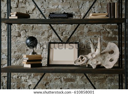 Frame mock up on shelf with books, globe, plaster dinosaur head, typing machine and educational items. Interior photo for display of your work