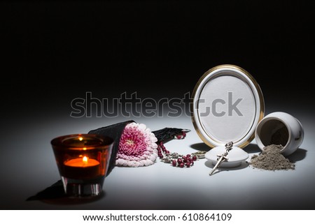 white urn with blank mourning frame, flower, candle and rosary on dark background for sympathy card