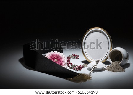 white urn with blank mourning frame, flower, tape, candle and rosary for sympathy card on dark background