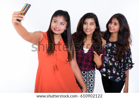 Studio shot of three happy young Persian woman friends smiling while taking selfie picture with mobile phone togther against white background