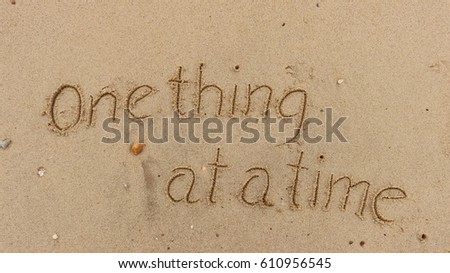 Handwriting words "One thing at a time" on sand of beach Royalty-Free Stock Photo #610956545