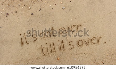 Handwriting words "it's not over till it's over." on sand of beach Royalty-Free Stock Photo #610956593