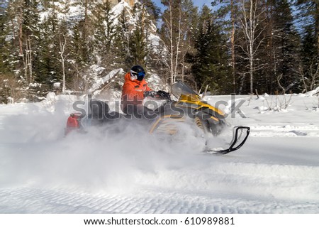 The sportsman on a snowmobile moving through deep snowdrifts in the winter forest in the mountains of the Southern Urals.