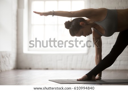 Side view portrait of young yogi woman practicing yoga concept, standing in Utthita Trikonasana exercise, extended triangle pose, working out, wearing sportswear, white loft studio background, closeup Royalty-Free Stock Photo #610994840