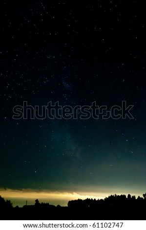 starry sky. clouds at the horizon lighting from the lights from a city. contours are visible from a wood.