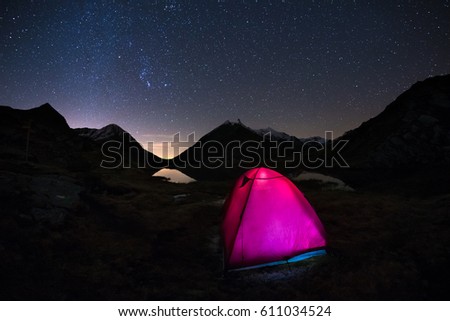 Camping under starry sky and Milky Way arc at high altitude on the italian french Alps. Glowing tent in the foreground. Adventure into the wild.

