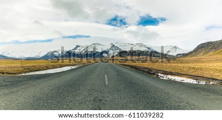 Empty countryside road in Iceland with mountains on background. Asphalt road through fields and wilderness on a cloudy day. Icelandic typical landscape. Travel and nature concepts