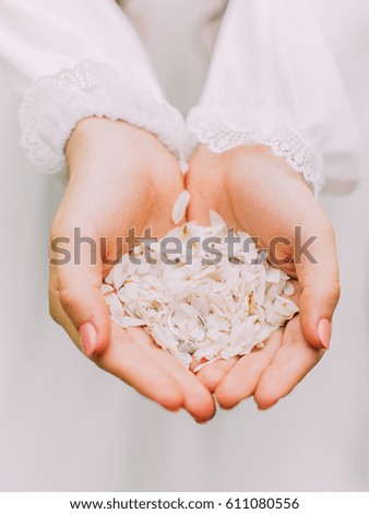 The close-up photo of the woman`s hand full of white petals holdding the wedding ring.