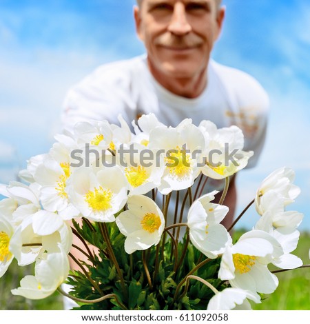 An elderly, handsome man holds out a bouquet of white flowers in his hands. Summer day. Selective focus